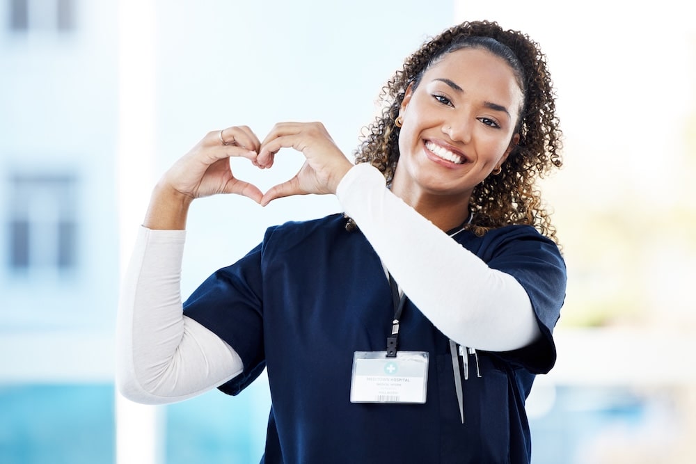 Smiling CNA nurse making a heart gesture, symbolizing compassion and the rewarding nature of a CNA career.
