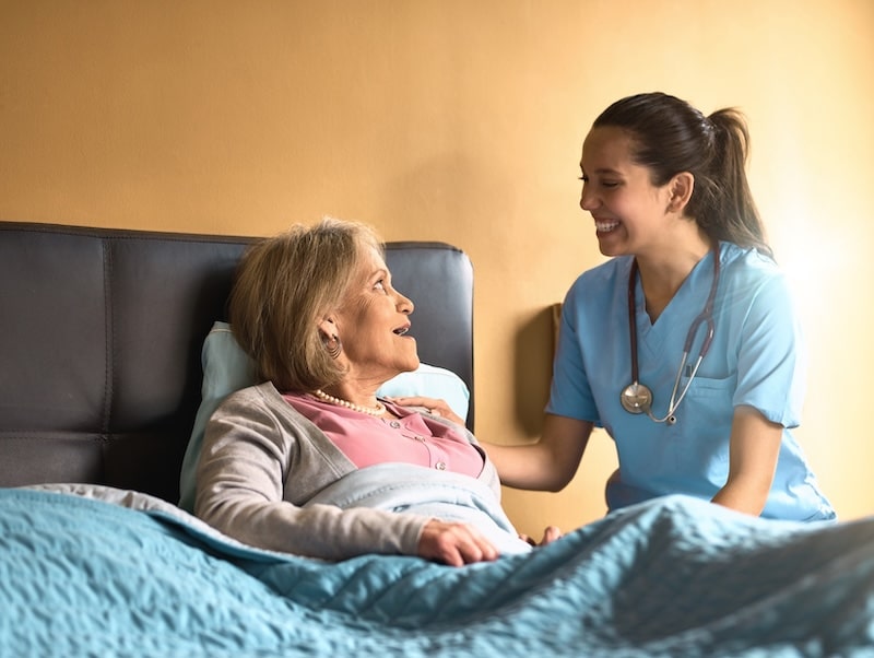 CNA providing care and emotional support to an elderly woman in bed