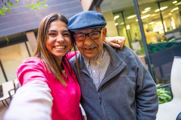 Young CNA smiling with elderly male patient outside an assisted living facility