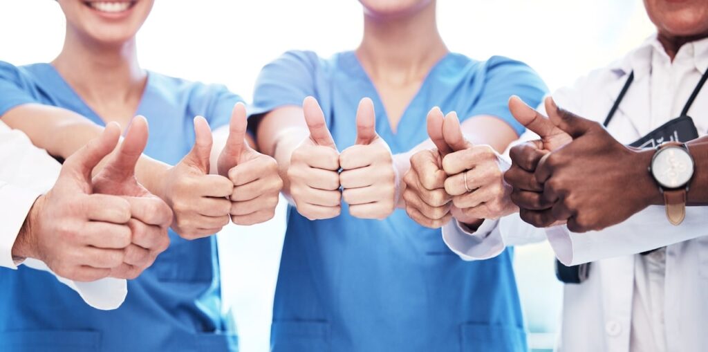Group of CNA students and healthcare professionals giving thumbs up in support of training success