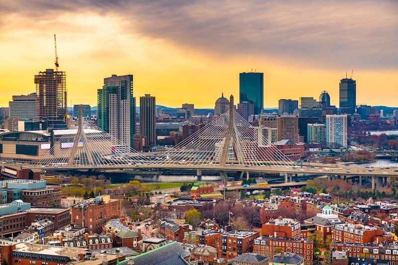 Aerial view of Boston skyline at sunset with the Leonard P. Zakim Bunker Hill Bridge in the foreground.