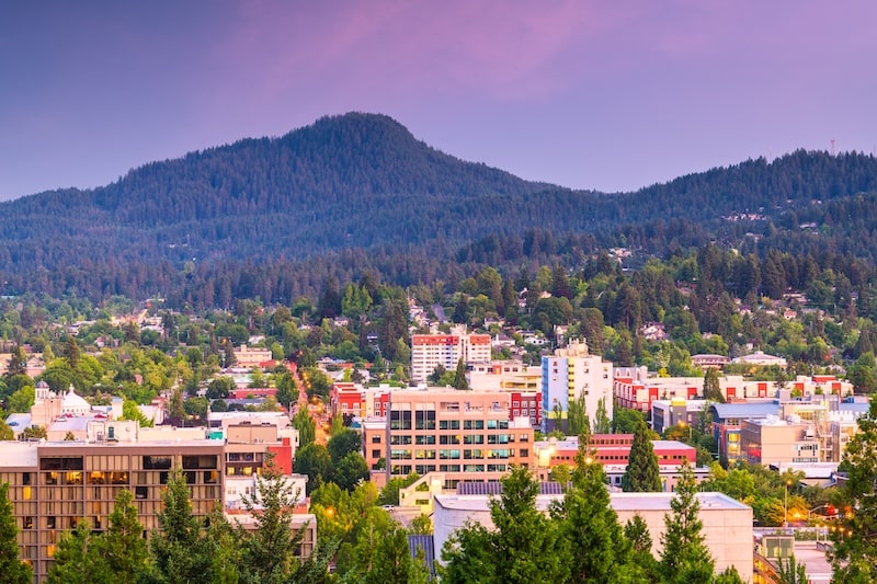 Downtown Eugene, Oregon city skyline with forested hills in the background at dusk.