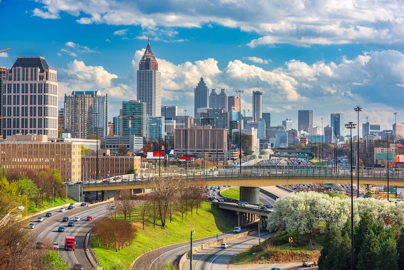Cityscape of downtown Atlanta, Georgia with freeway traffic and skyline under a partly cloudy sky.