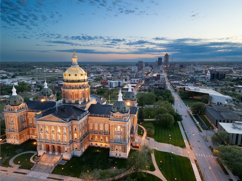 Aerial view of the Iowa State Capitol in Des Moines with the city skyline in the background at dusk.