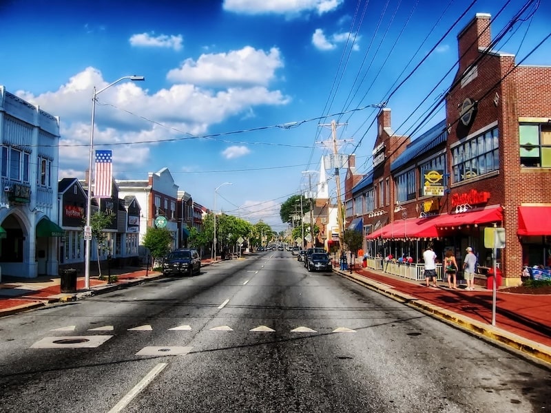 A wide view of Main Street in Newark, Delaware, showing local shops, pedestrians, and historic brick buildings under a bright blue sky.