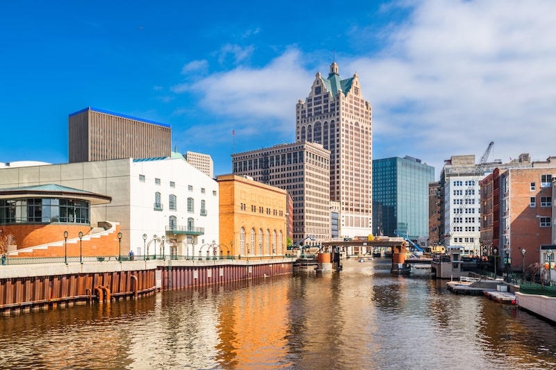 Downtown Milwaukee, Wisconsin skyline view with river and buildings under a blue sky.