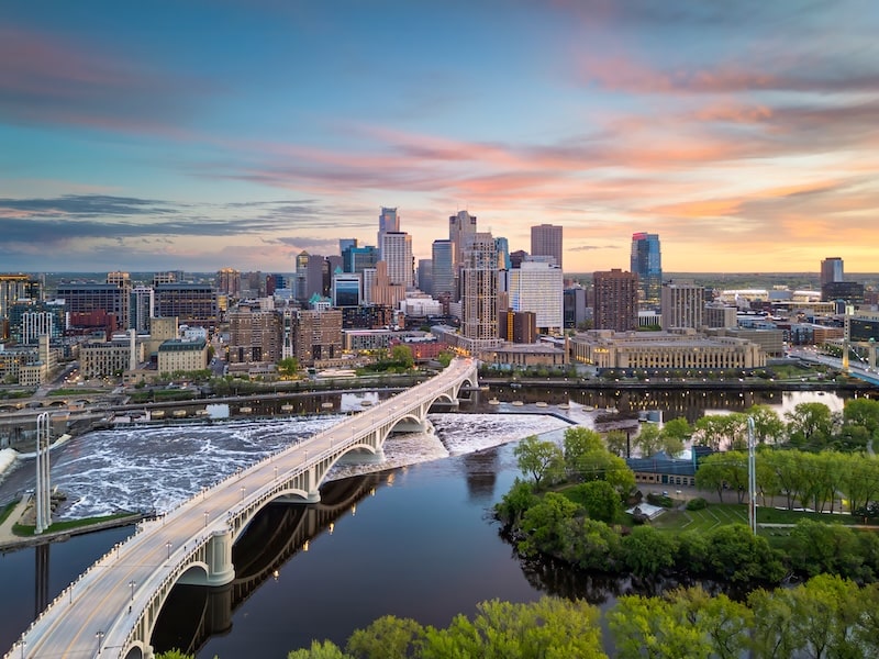 Downtown Minneapolis skyline with a view of the Mississippi River and Stone Arch Bridge at sunset.