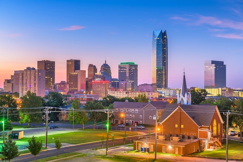 Evening view of the Oklahoma City skyline with illuminated buildings and a church in the foreground.