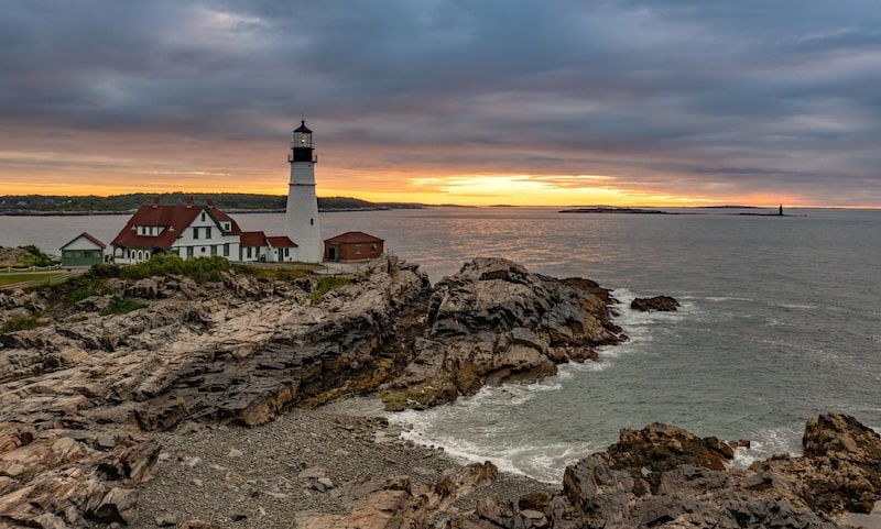 Portland Head Lighthouse on rocky Maine coastline during sunset
