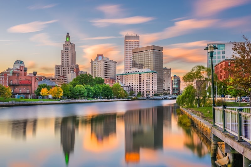 Skyline view of downtown Providence, Rhode Island, with colorful buildings reflecting in the river at sunset.
