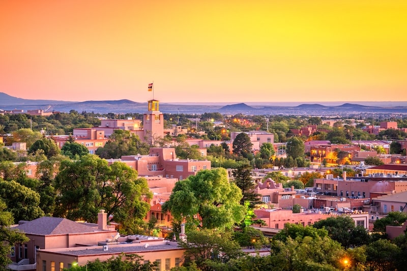Sunset over downtown Santa Fe, New Mexico, showcasing adobe-style buildings and a scenic desert landscape.