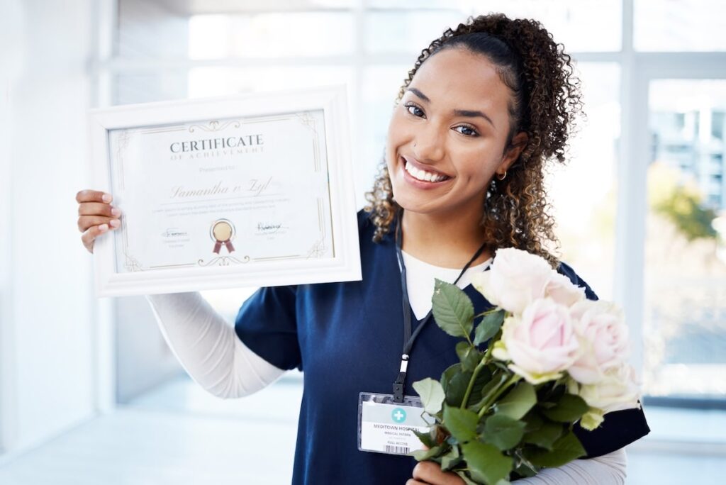 Smiling CNA graduate holding a certificate of achievement and flowers after completing training.